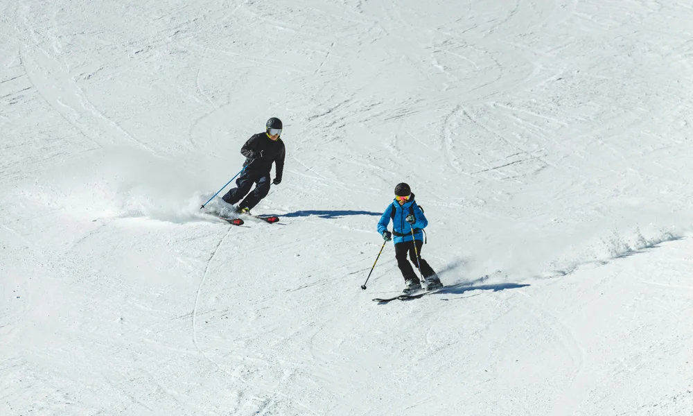 Zwei Skifahrer fahren auf schneebedeckter Piste bei Sonnenschein