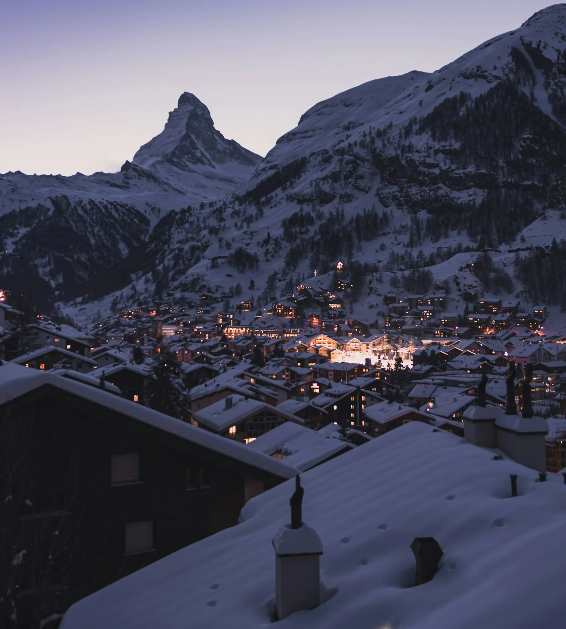 acotar Schneebedeckte Dächer eines Bergdorfs mit beleuchtetem Matterhorn im Hintergrund bei Dämmerung