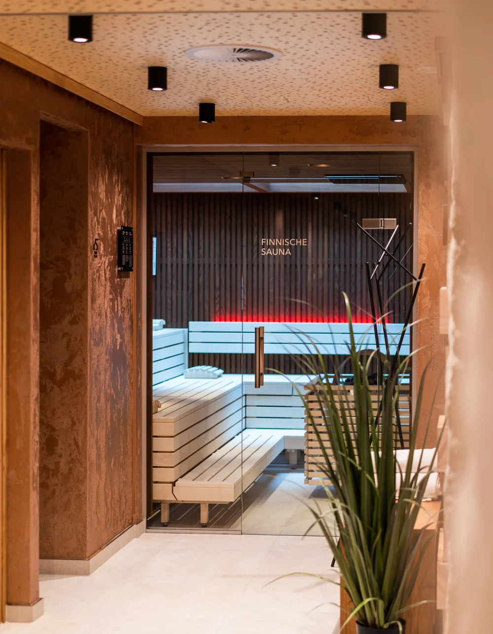 Eingang zur Finischen Sauna mit roter Beleuchtung und Pflanze im Vordergrund