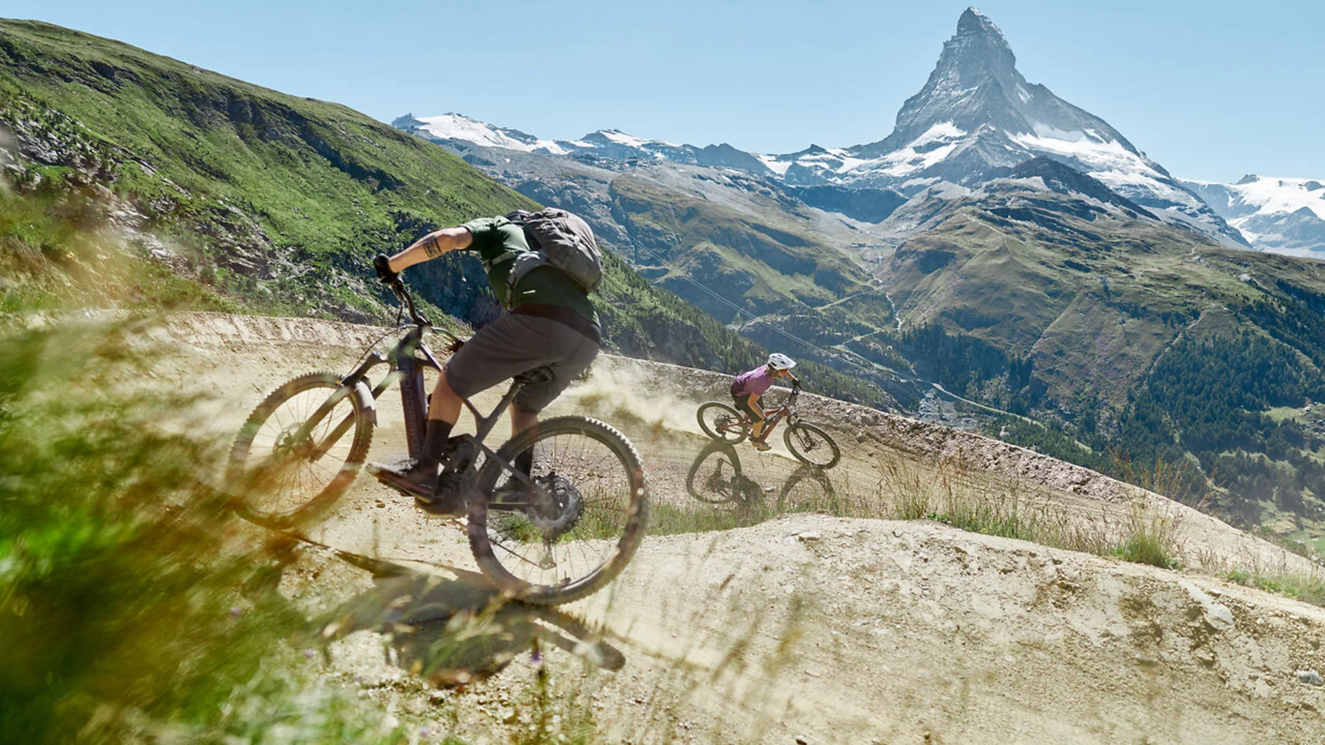 Zwei Mountainbiker fahren auf bergigem Weg mit Matterhorn im Hintergrund