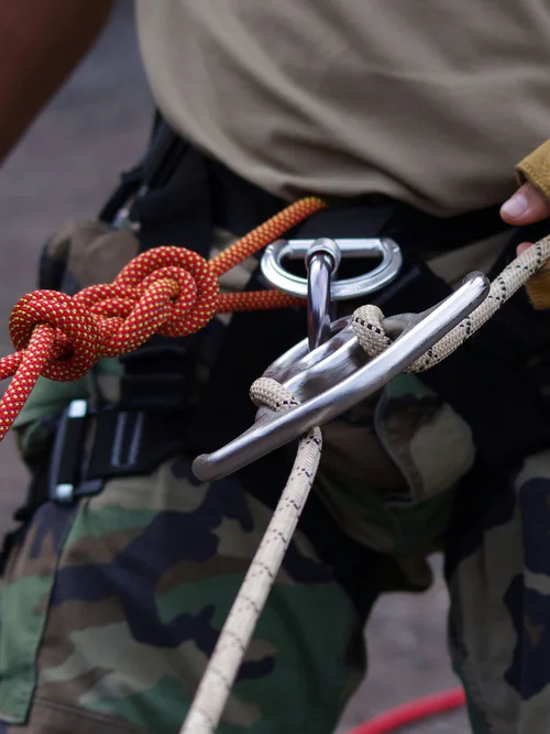 Person mit Kletterausrüstung und Handschuhen hält Seile und Karabiner