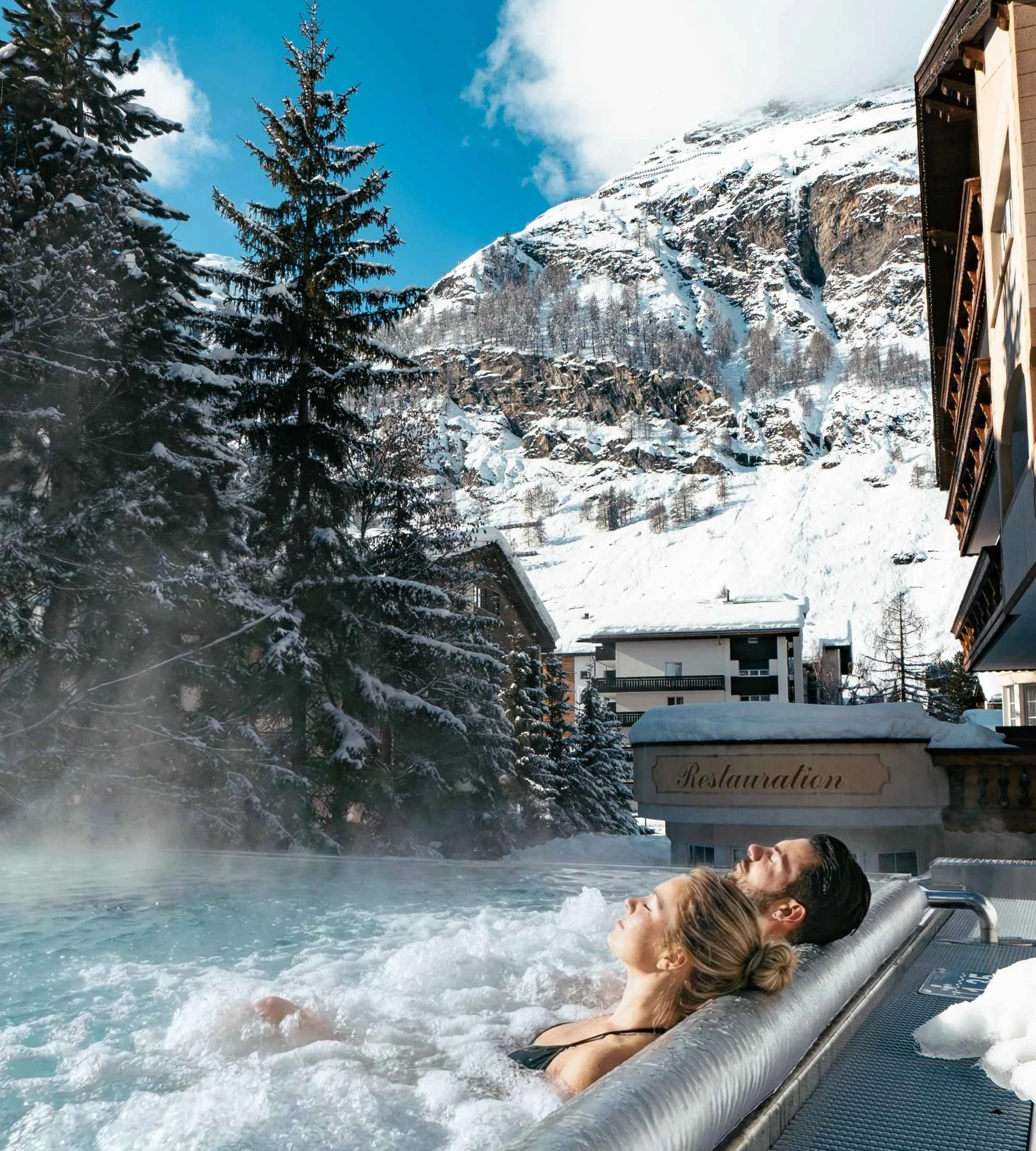 Menschen im Infinitypool mit Massagedüsen und Aussicht auf die verschneiten Berge im Winter.