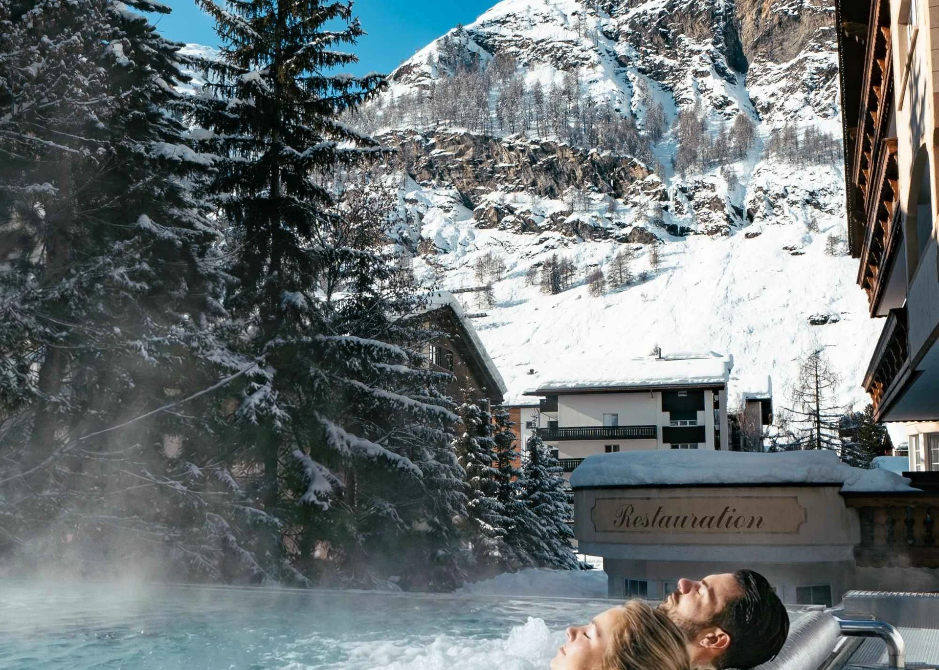 Des personnes dans la piscine à débordement avec jets de massage et vue sur les montagnes enneigées en hiver.