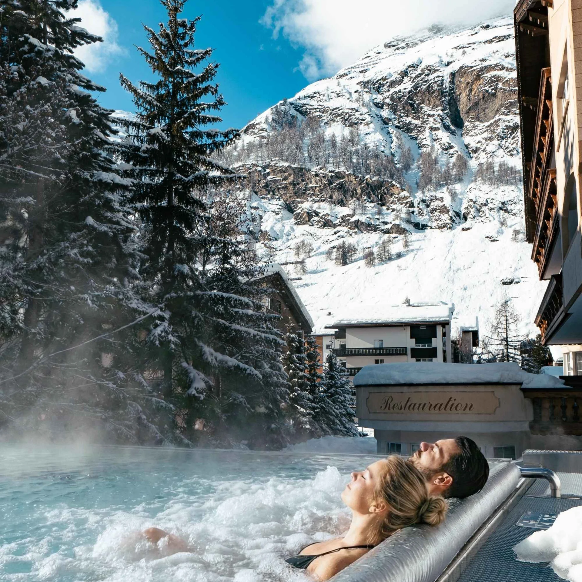 Des personnes dans la piscine à débordement avec jets de massage et vue sur les montagnes enneigées en hiver.