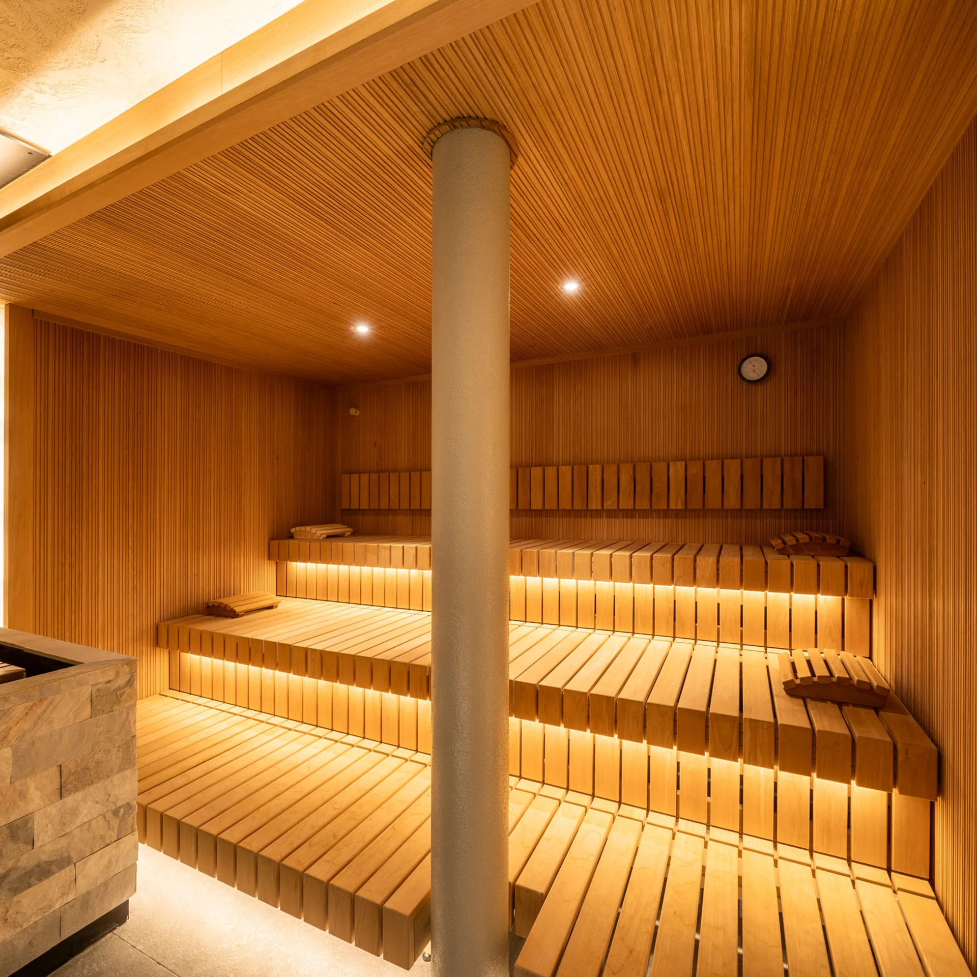 Moderner Holzsauna mit beleuchteten Bänken und Steinofen