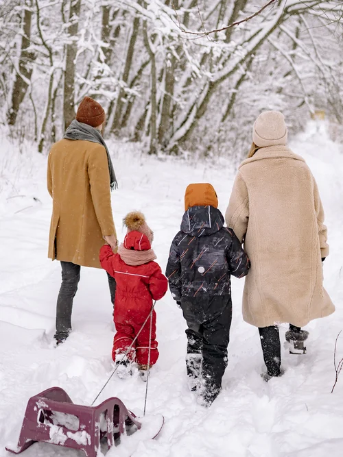 Zwei Erwachsene und zwei Kinder gehen mit einem Schlitten durch einen verschneiten Wald