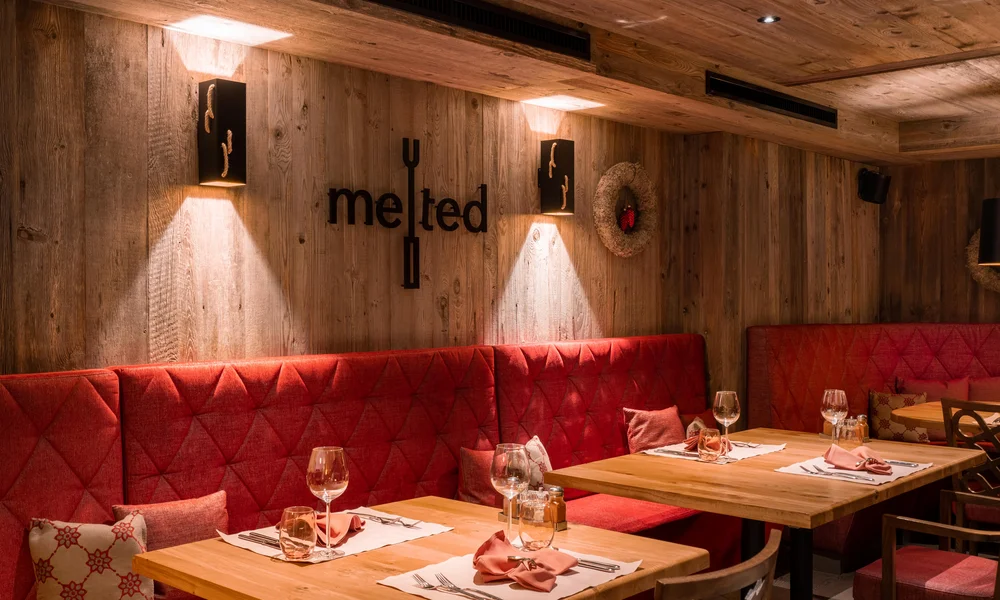 Käsestube melted - Resort La Ginabelle Zermatt Gemütliches Restaurantambiente mit Holzverkleidung und roten Polstern.