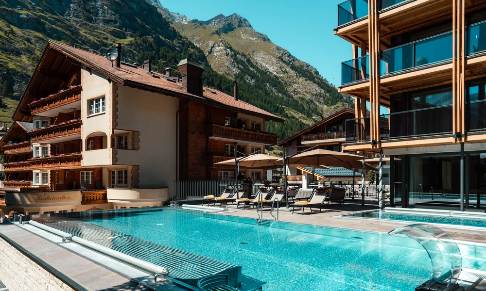 Infinitypool mit Terrasse und Bergen im Hintergrund im Sommer.