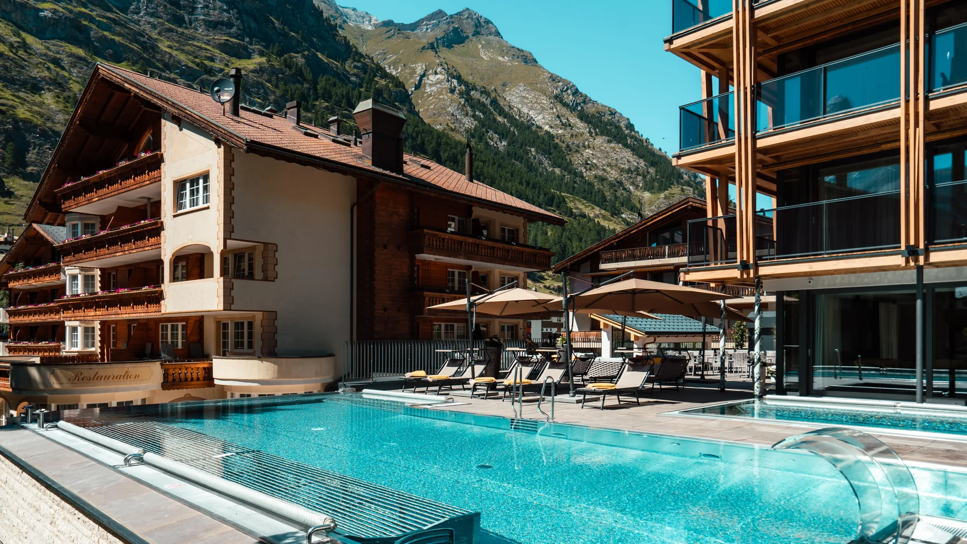 Infinity pool with terrace and mountains in the background in summer.