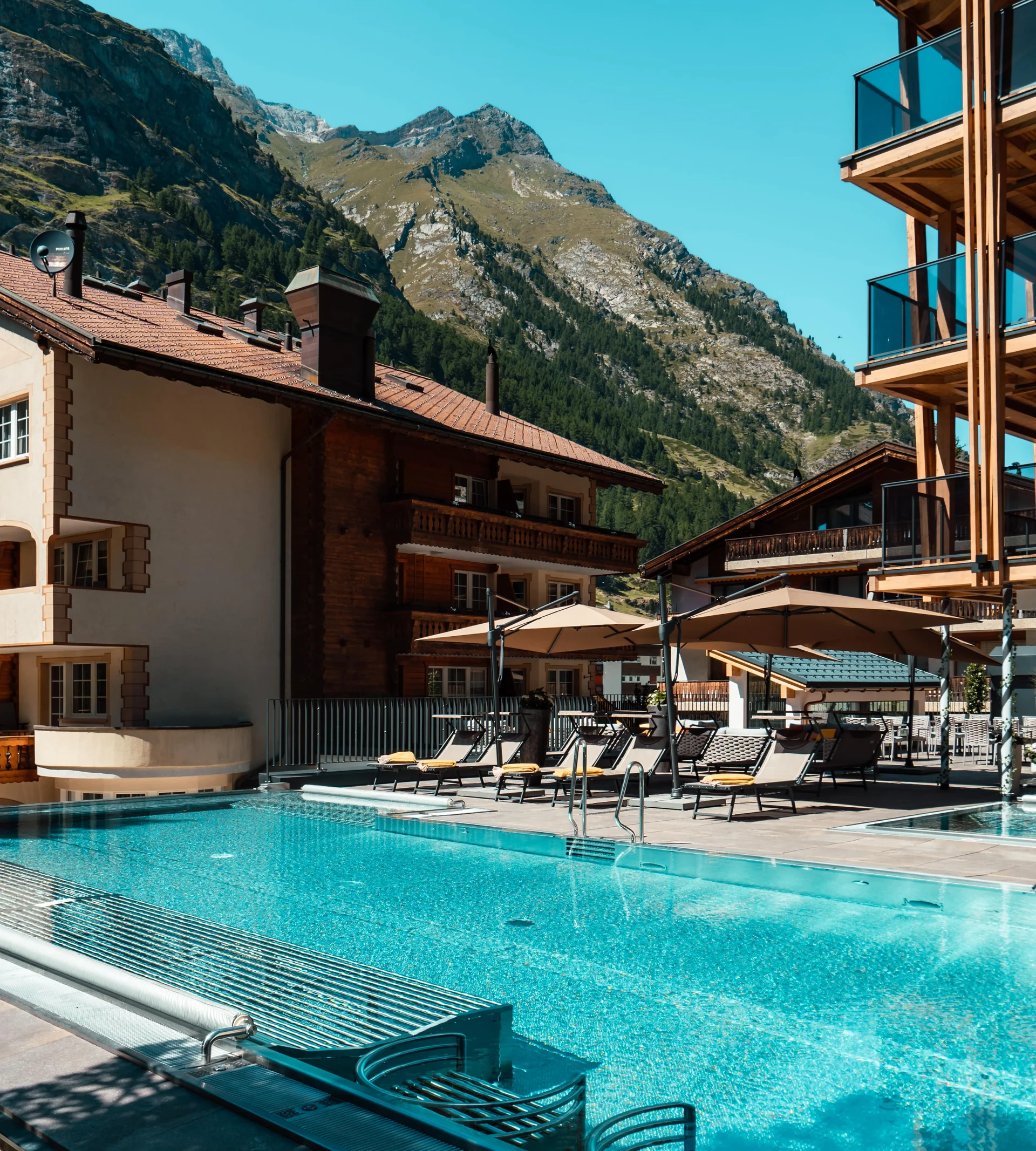 Infinitypool mit Terrasse und Bergen im Hintergrund im Sommer.