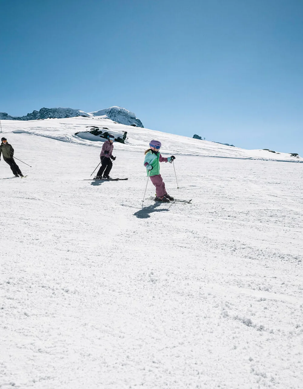 Quatre skieurs descendent une pente enneigée sous un ciel bleu clair