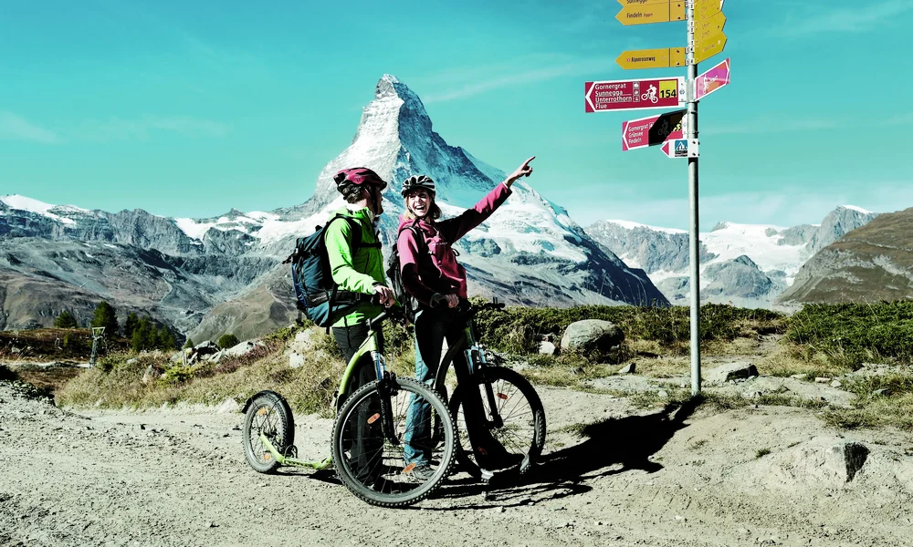 Location & Arrival - Resort La Ginabelle Zermatt Two people on the bicycle in front of the Matterhorn.
