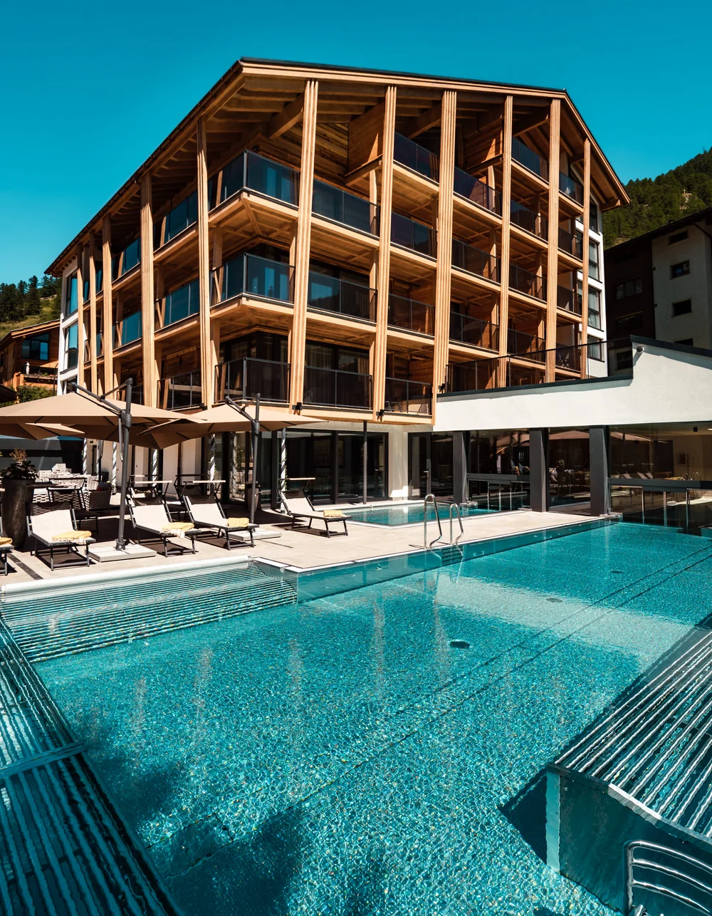Ferienwohnungen Hotelservice - Resort La Ginabelle Zermatt Gebäude im Sommer mit grossem Aussenpool und Ruheliegen.