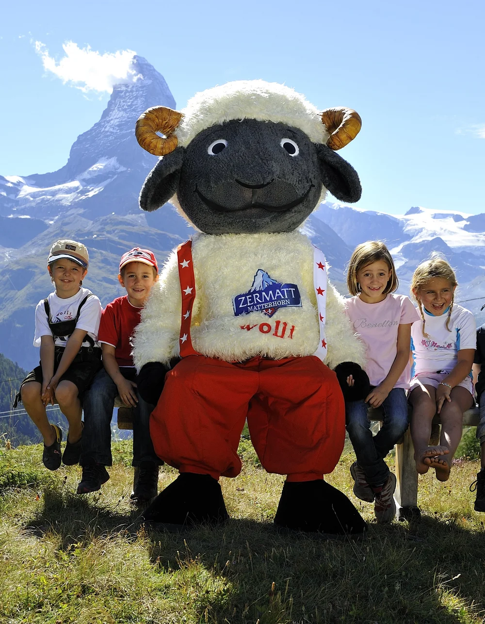 Gruppe von Kindern mit Maskottchen Wolli in den Bergen