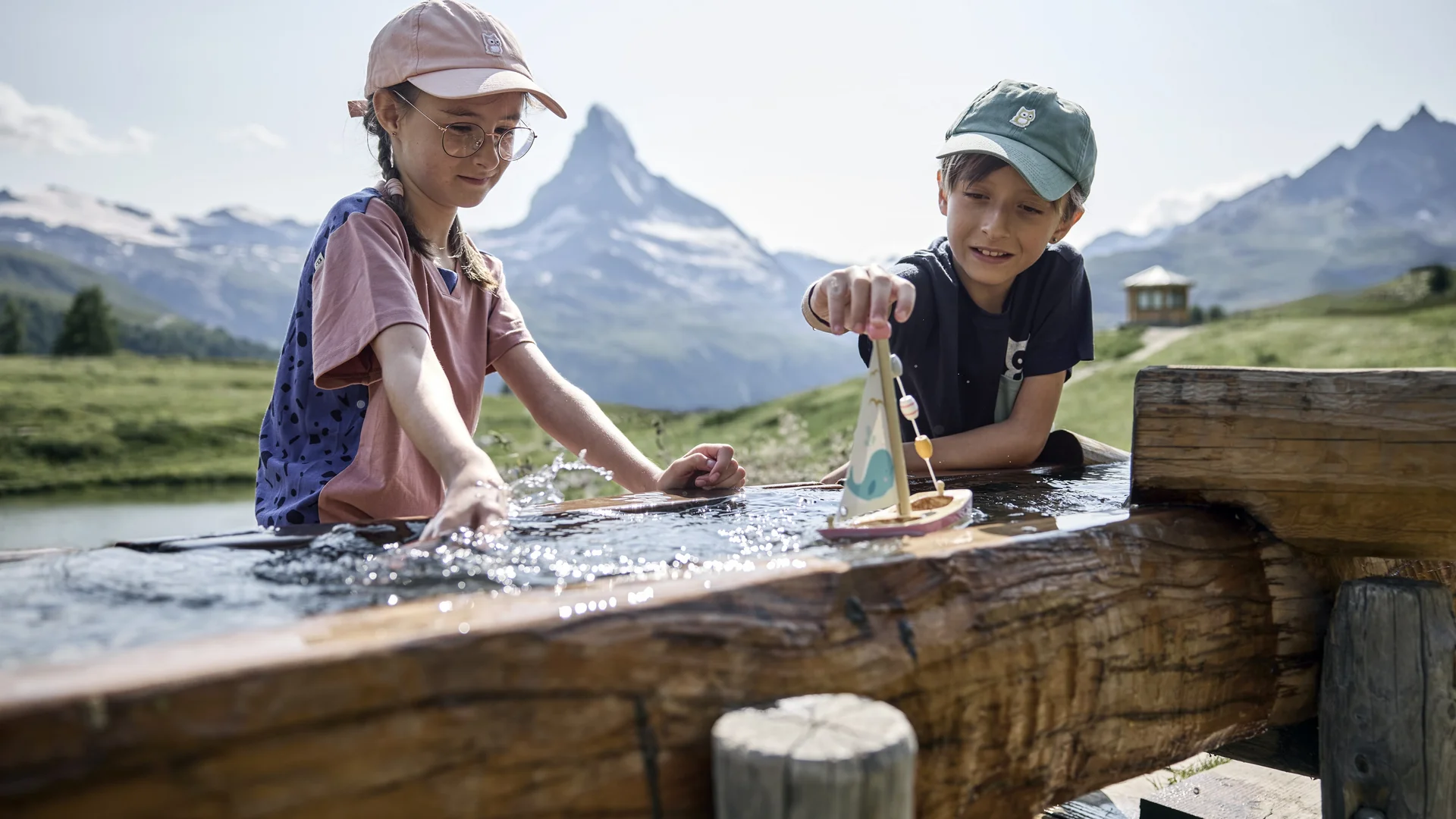 Ferien mit Kindern in Zermatt - Resort La Ginabelle Zermatt Kinder spielen an einem Brunnen mit dem Matterhorn im Hintergrund und klarem Himmel