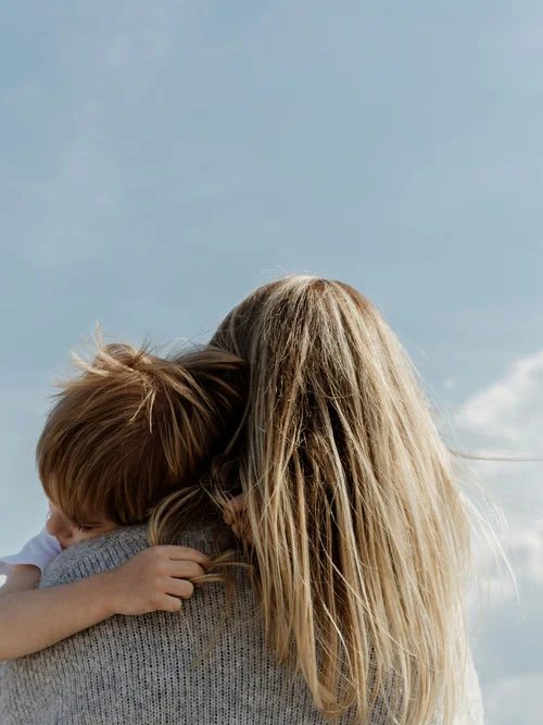 Kind liegt schlafend auf der Schulter einer Person mit langen blonden Haaren
