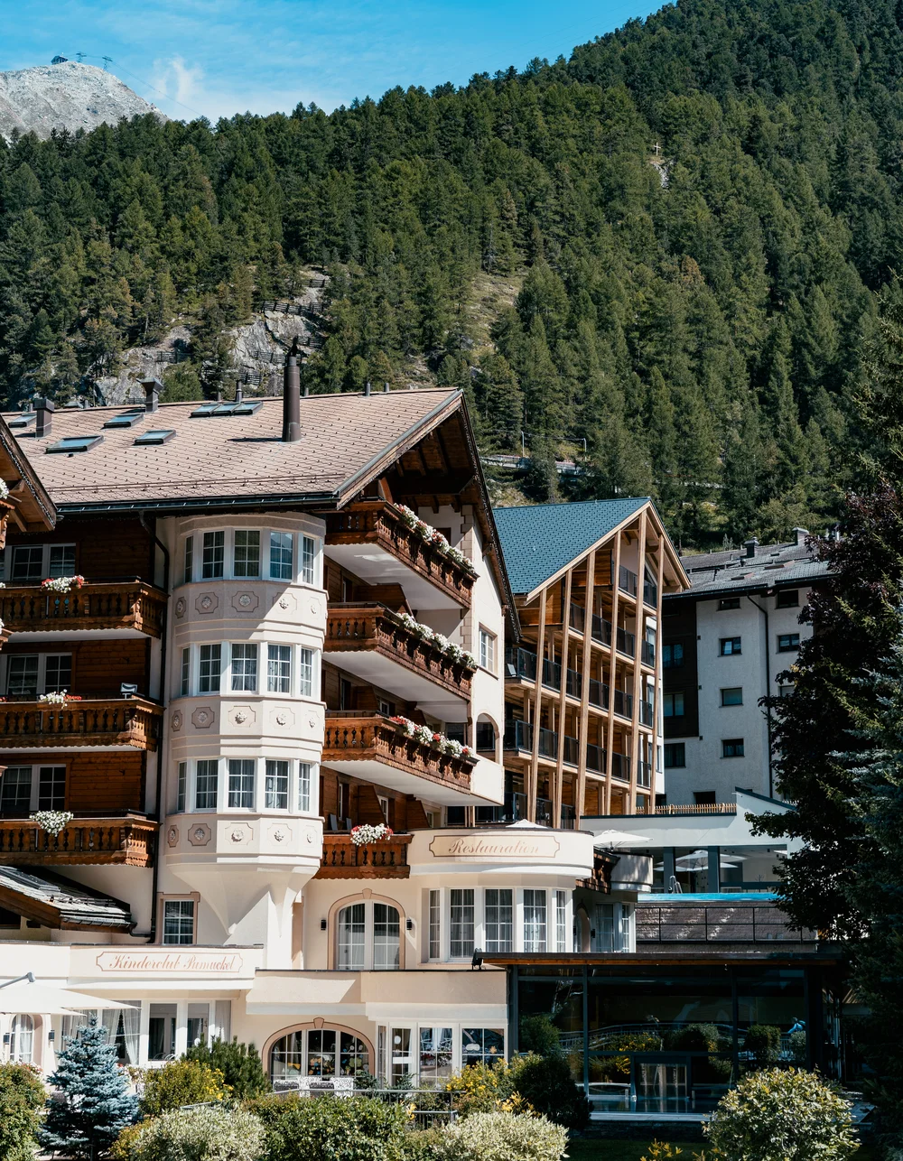 acotar Hotelgebäude mit Balkon und Bergen im Hintergrund unter blauem Himmel