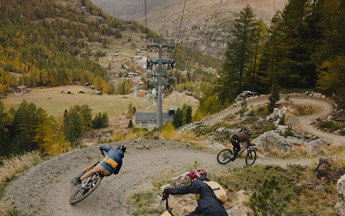 Drei Mountainbiker fahren auf einem kurvigen Bergpfad in herbstlicher Landschaft