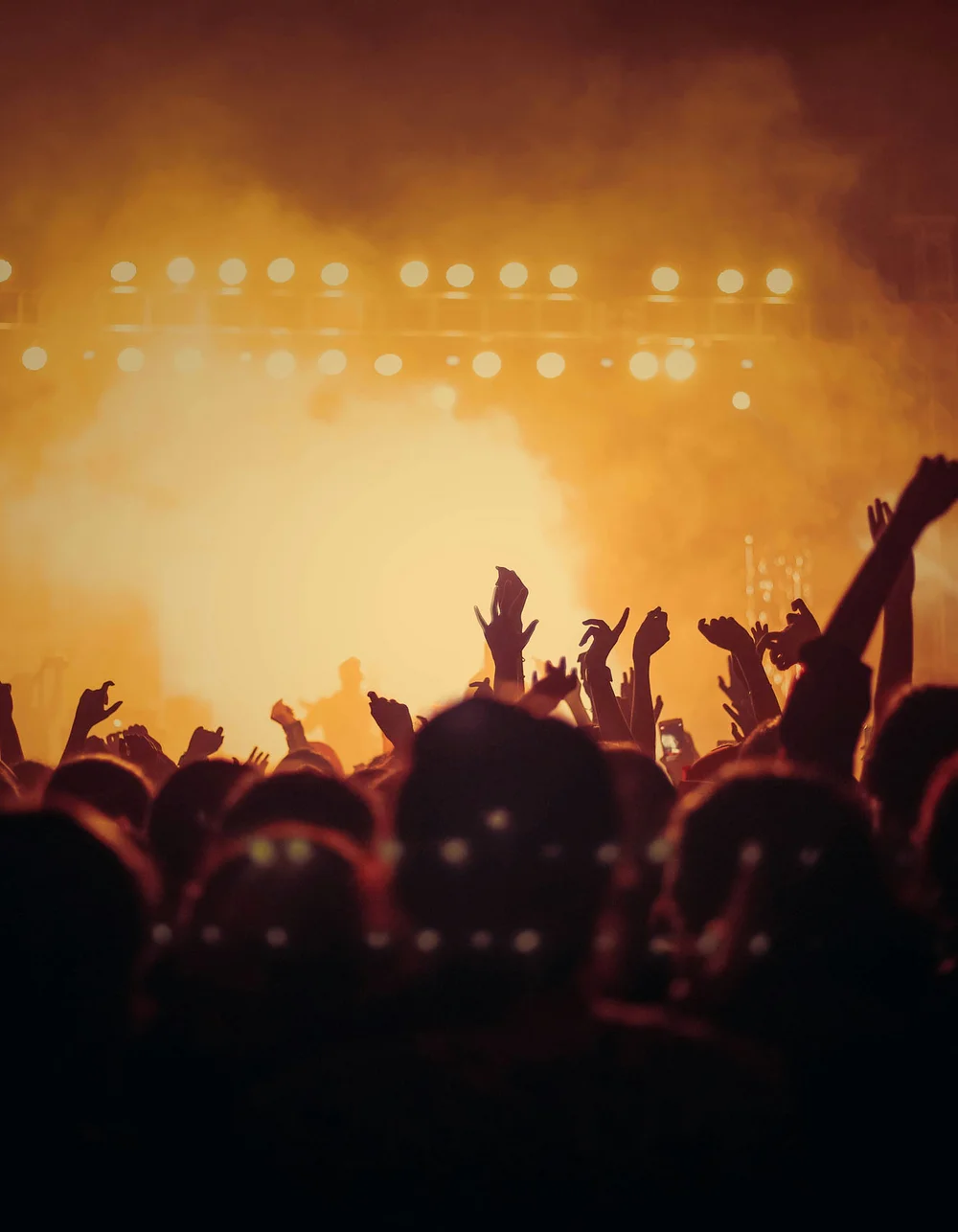 Crowd at concert with raised hands in front of brightly lit stage background