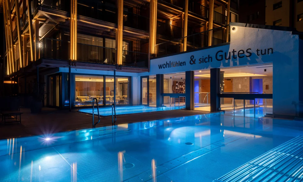 Beleuchteter Infinitypool mit beleuchtetem Hotel im Hintergrund in der Nacht.