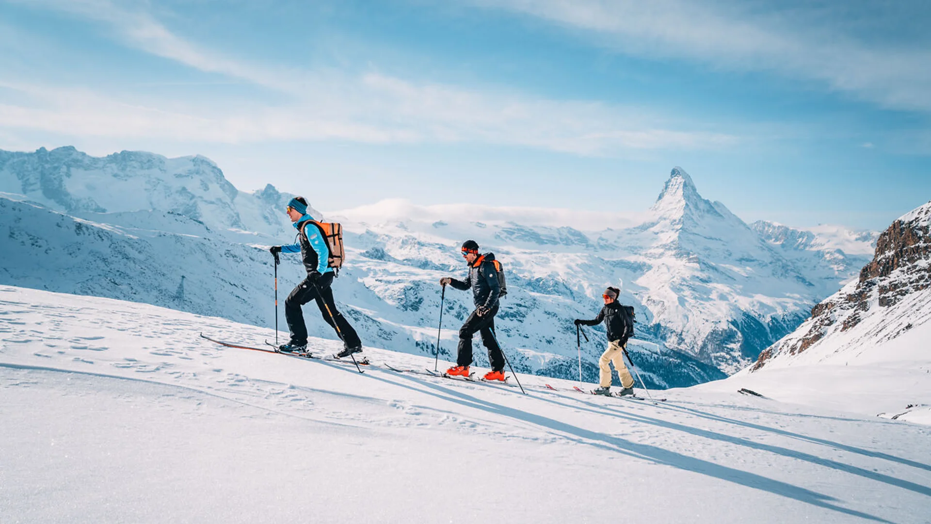 Wintersport Vier Skifahrer wandern im Schnee vor schneebedeckten Bergen und blauem Himmel