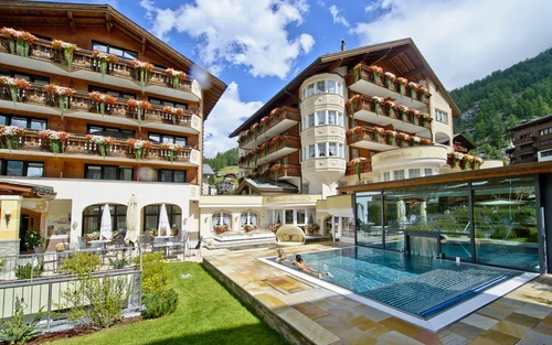Hotel mit Aussenpool und Garten im Sommer bei schönem Wetter.