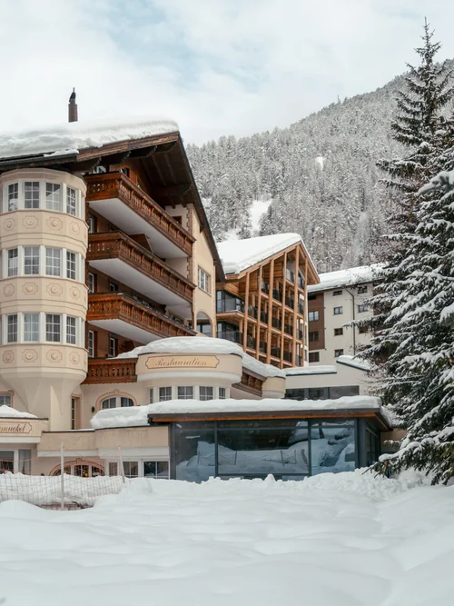 Snow-covered hotel with outdoor pool with snow-covered forest in the background.