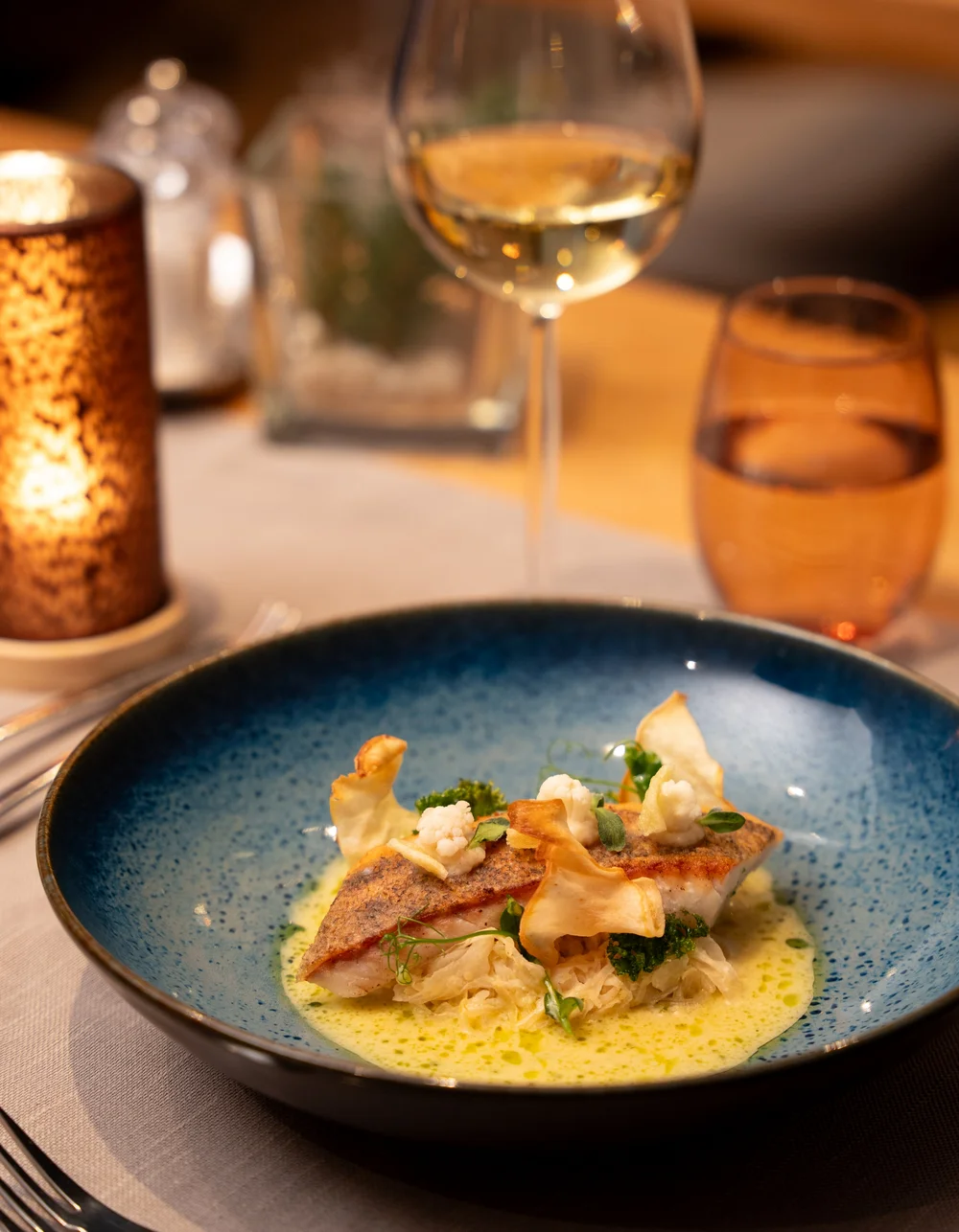 Restaurant La Ginabelle - Resort La Ginabelle Zermatt Gebratener Fisch mit Safransauce angerichtet auf einem blauen Teller und einem Glas Wein