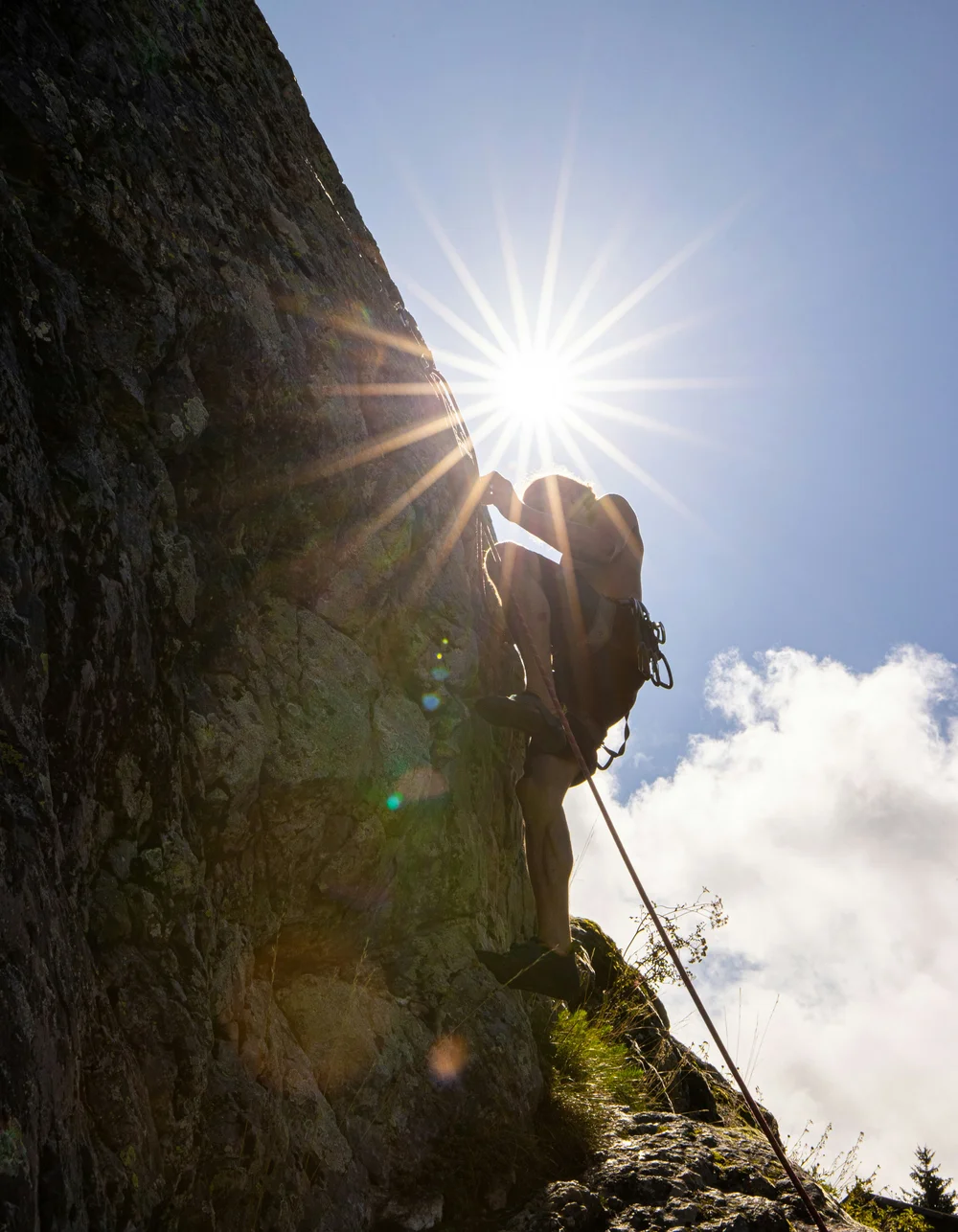 Klettern & Bergsteigen Kletterer klettert Felsen im Sonnenschein mit Sicherungsseil