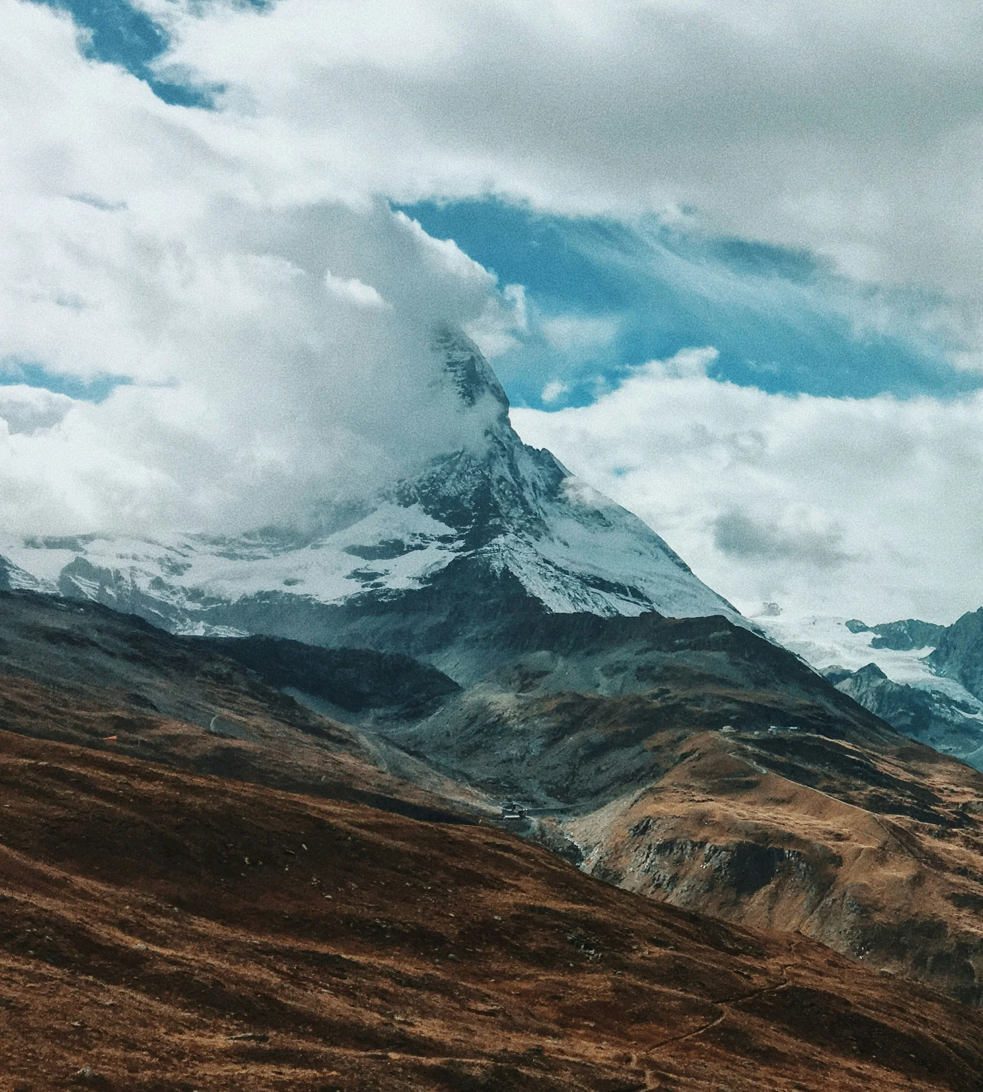 Klettern & Bergsteigen Schneebedeckter Berg teilweise von Wolken verdeckt über braunen Hügeln