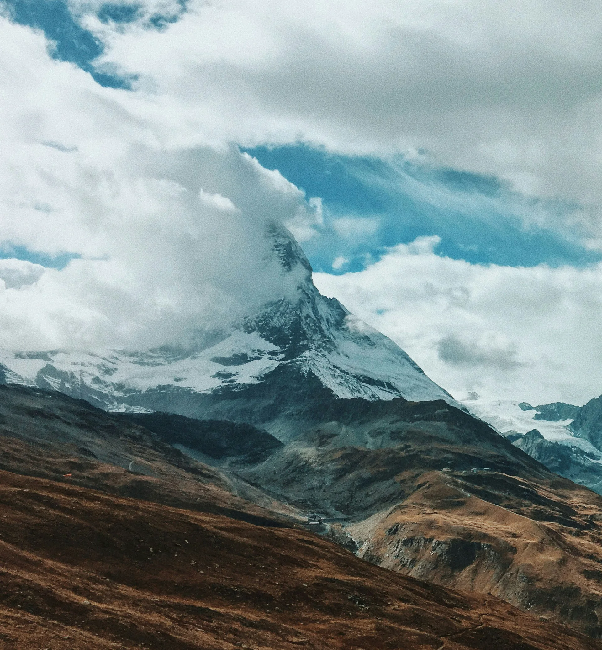 Schneebedeckter Berg teilweise von Wolken verdeckt über braunen Hügeln