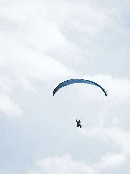 Aktivurlaub in den Bergen - Resort La Ginabelle Zermatt Person beim Gleitschirmfliegen hoch am Himmel mit Wolken