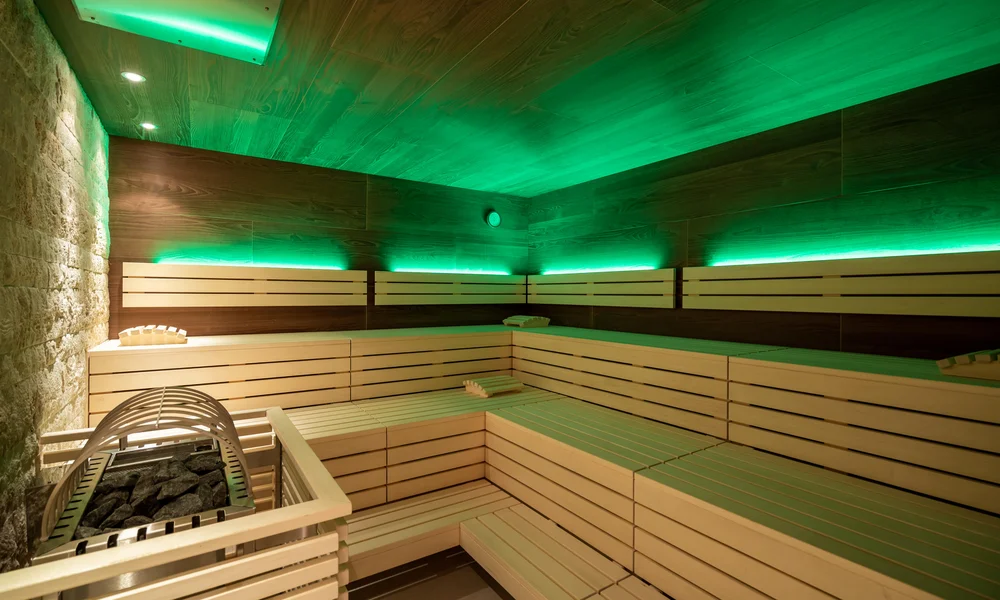 Bio Sauna mit indirekter grüner Beleuchtung, Holzbänken und in Holz verkleiderter Ofen.
