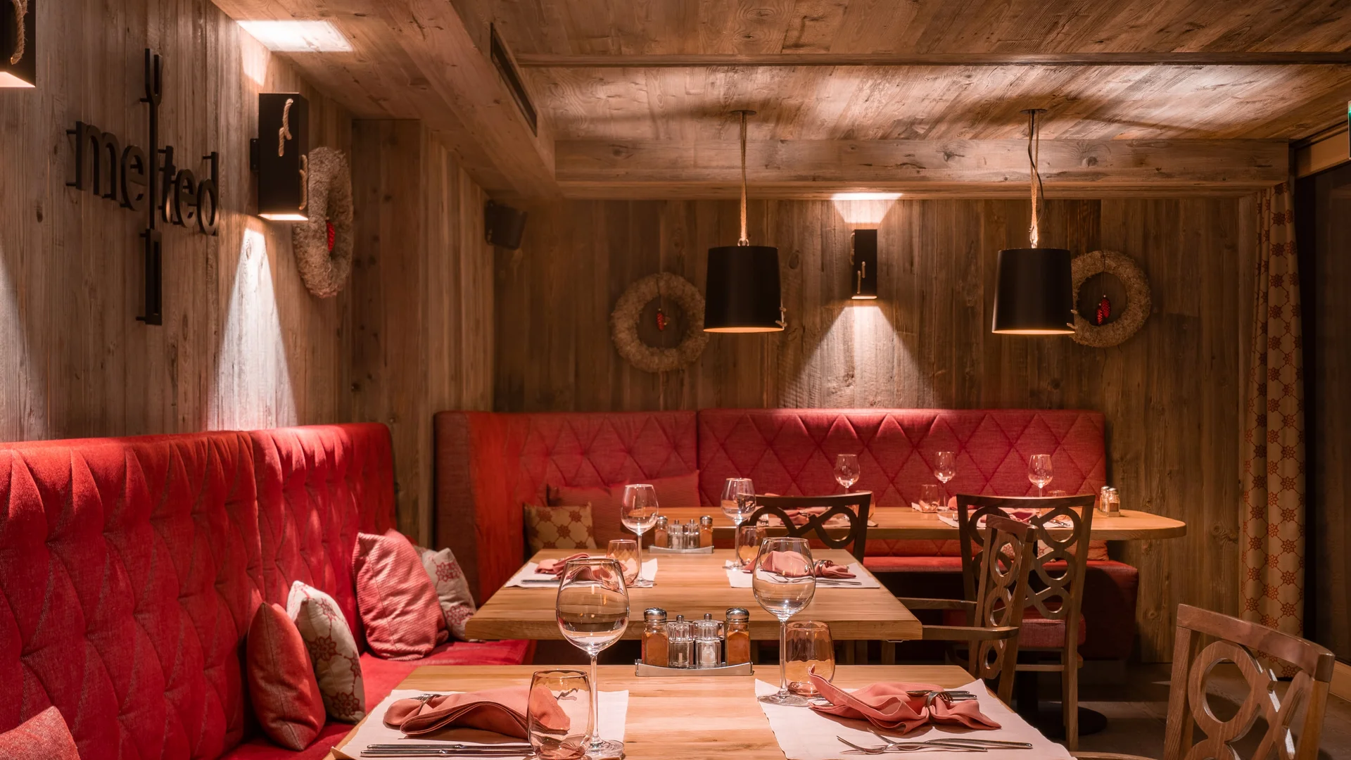 Käsestube melted - Resort La Ginabelle Zermatt Gemütliches Restaurantambiente mit Holzverkleidung und roten Polstern.