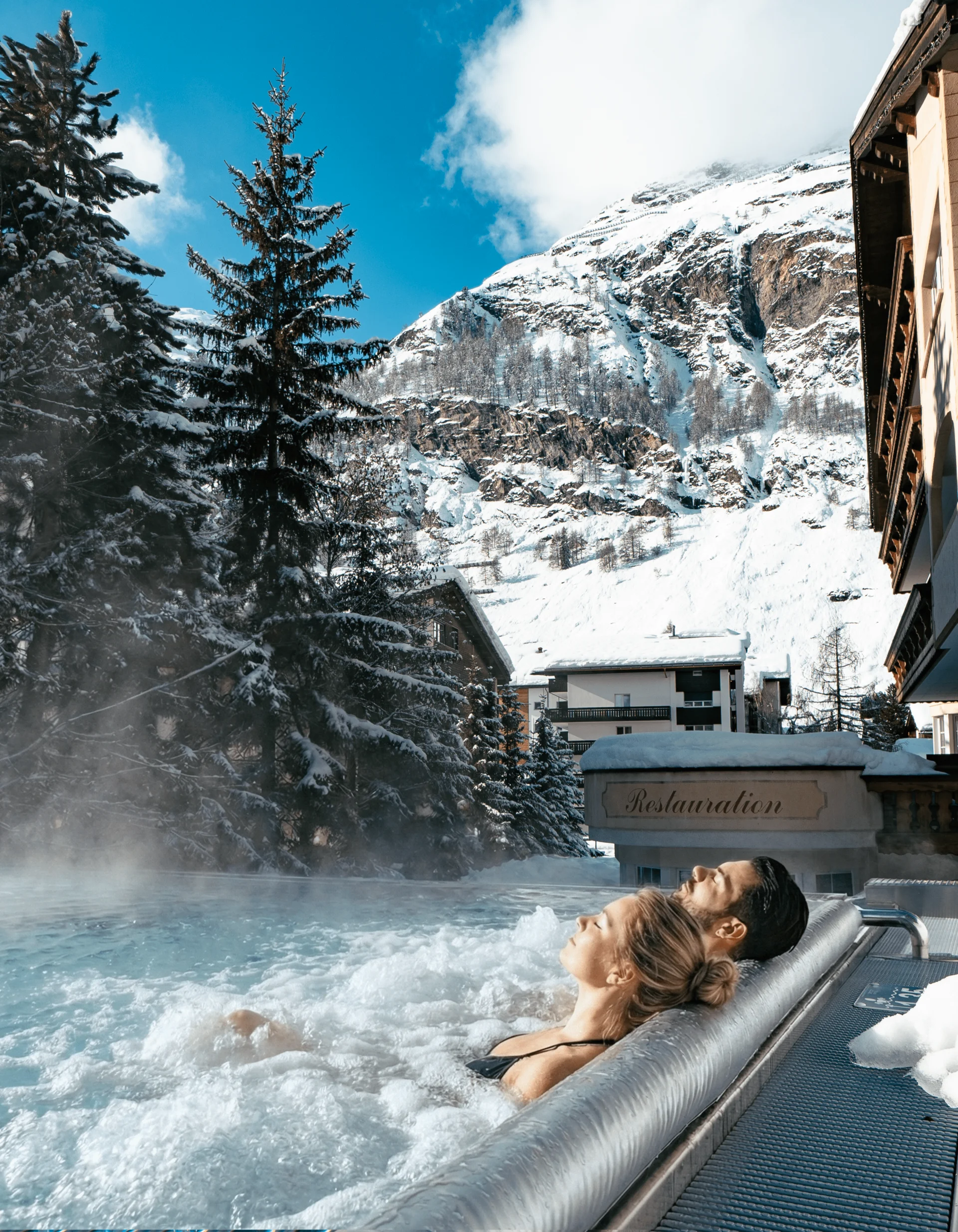 acotar Menschen im Infinitypool mit Massagedüsen und Aussicht auf die verschneiten Berge im Winter.