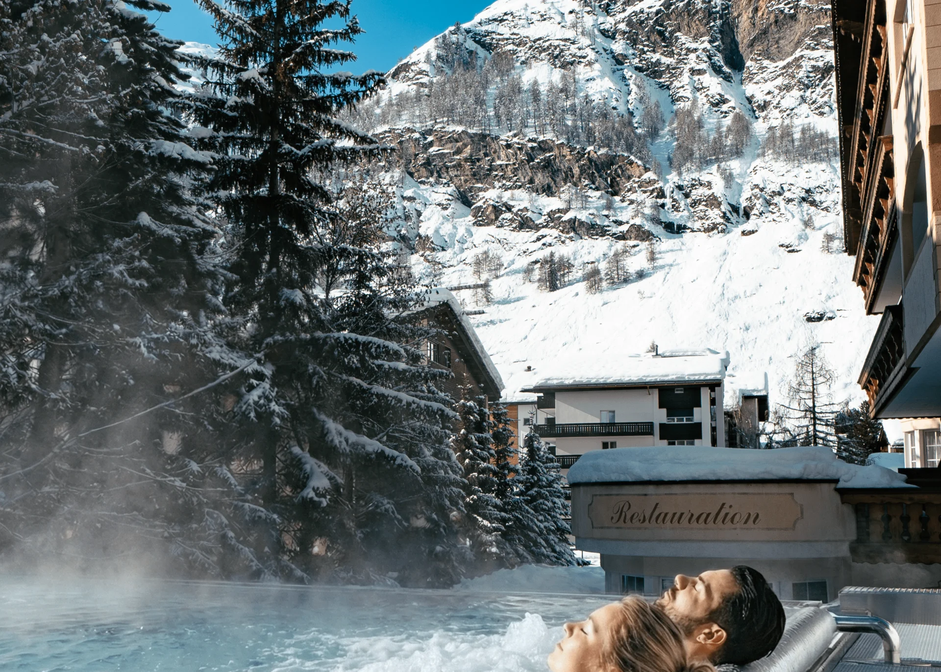 Menschen im Infinitypool mit Massagedüsen und Aussicht auf die verschneiten Berge im Winter.