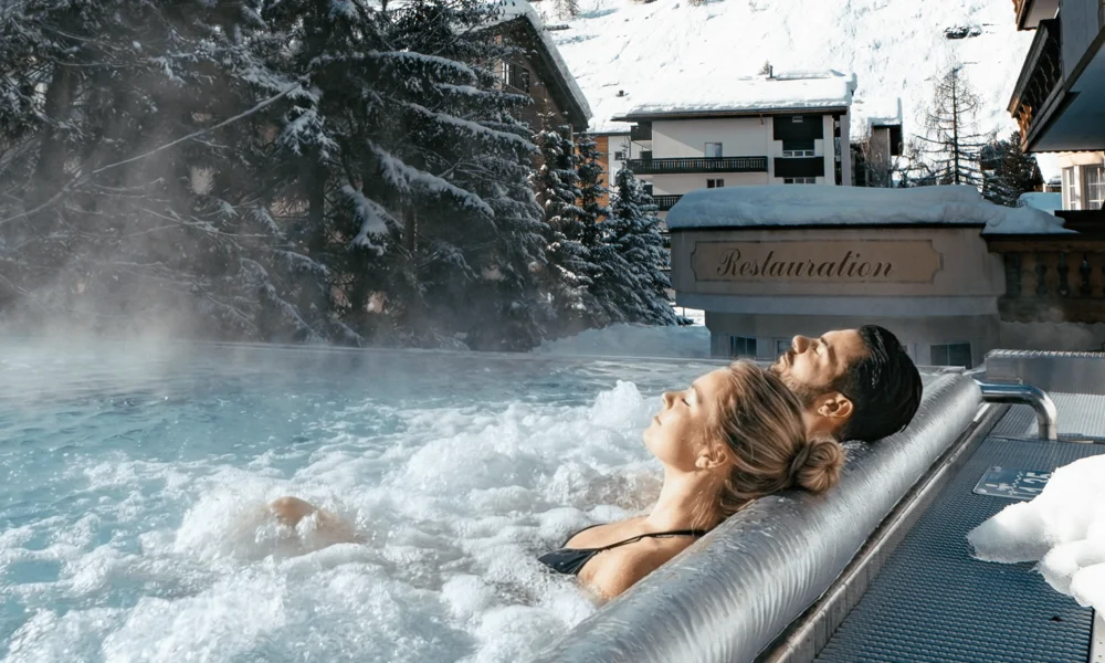 Die Wohlfühl-Wasserwelt - Resort La Ginabelle Zermatt Menschen im Infinitypool mit Massagedüsen und Aussicht auf die verschneiten Berge im Winter.