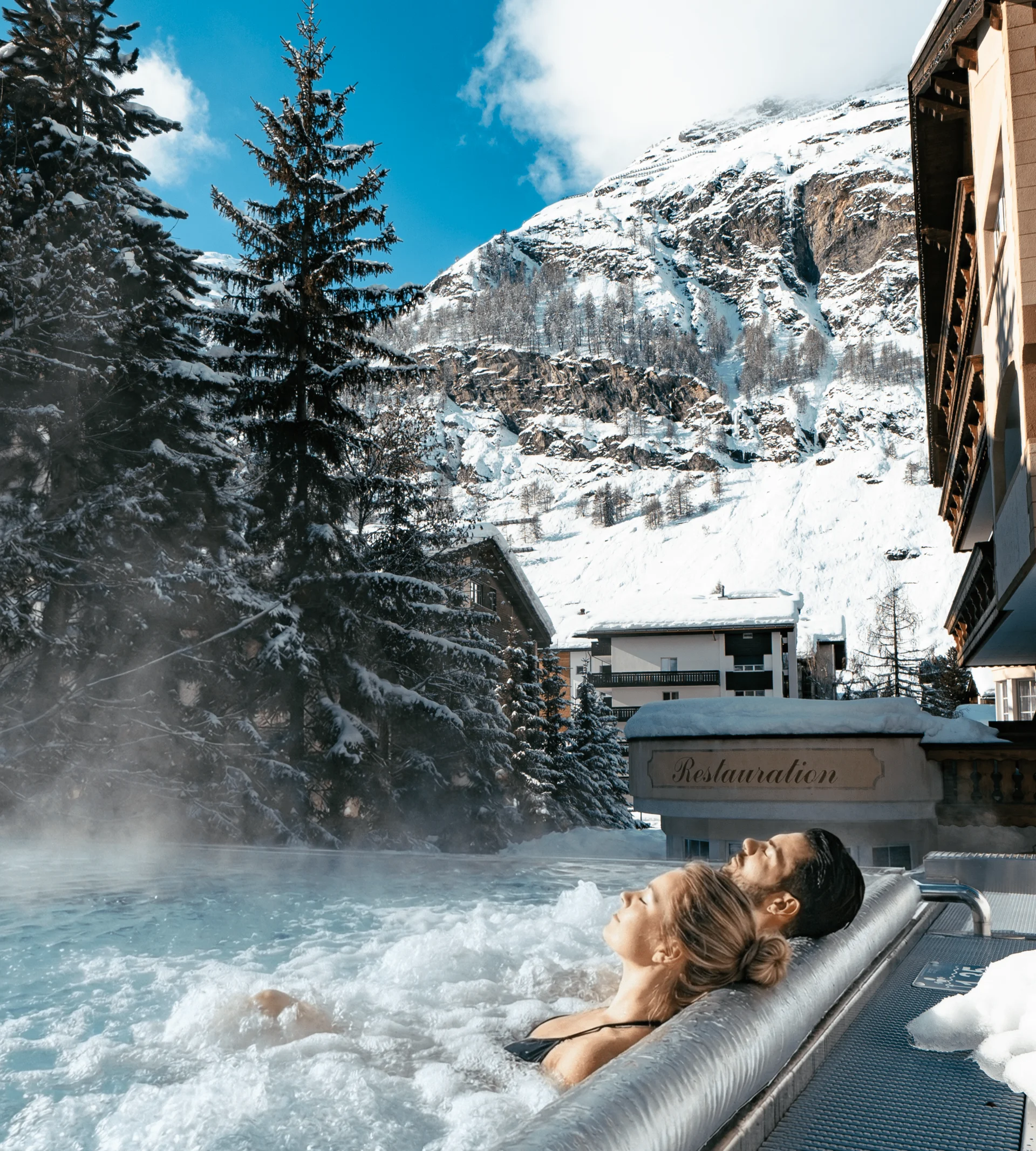 Des personnes dans la piscine à débordement avec des buses de massage et une vue sur les montagnes enneigées en hiver.