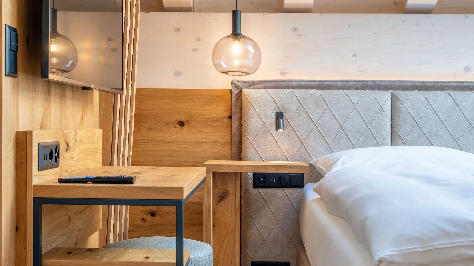 Resort La Ginabelle Zermatt: Ihr 4*S Wellnessresort in Zermatt Moderner Hotelzimmerbereich mit Holzmöbeln, Bett und TV an der Wand