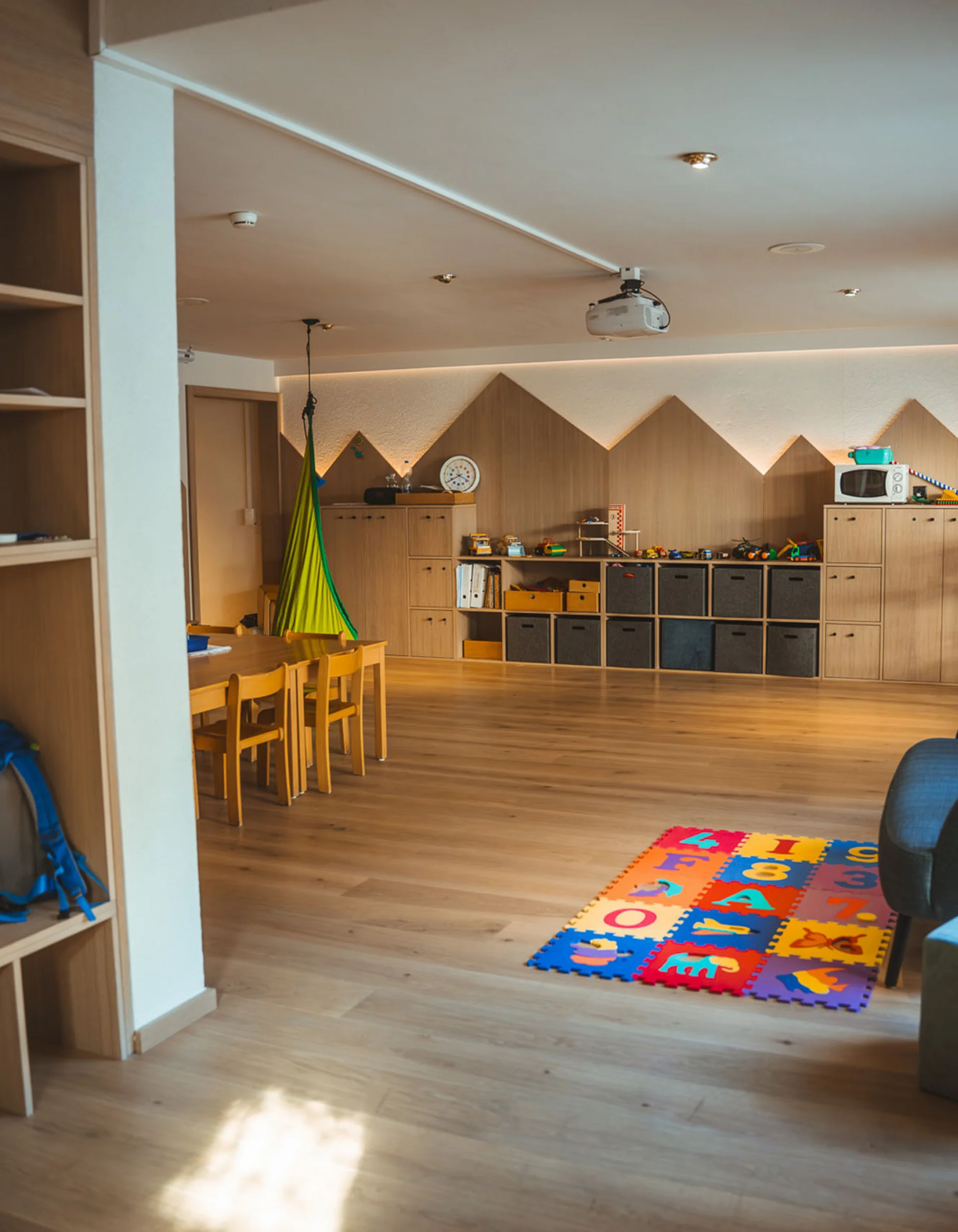 Kinderspielzimmer mit Holzregalen, Spielzeug und bunter Spielmatte