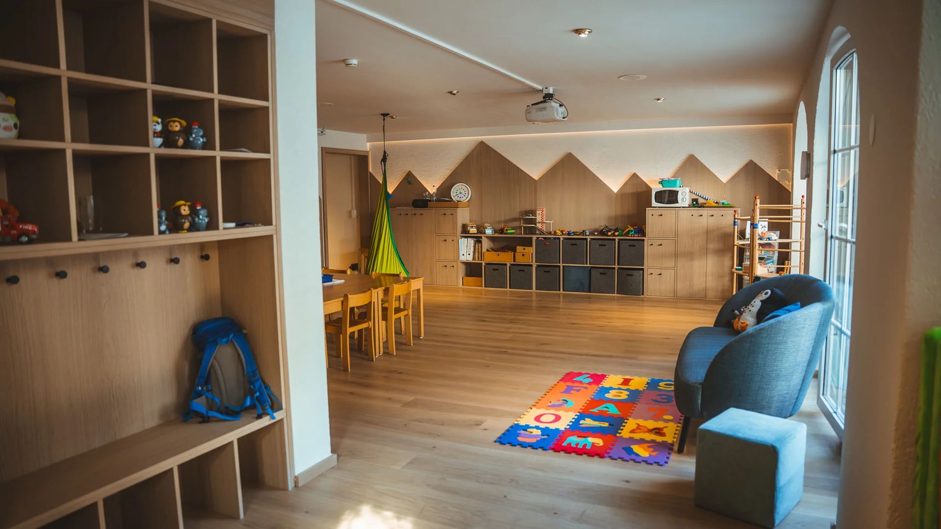 Kinderspielzimmer mit Holzregalen, Spielzeug und bunter Spielmatte