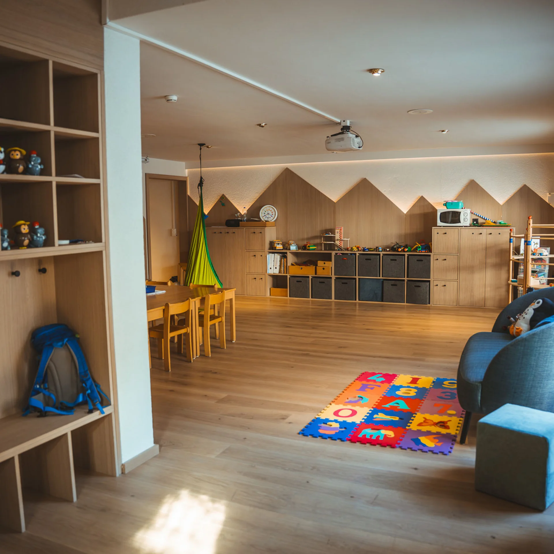 Kinderspielzimmer mit Holzregalen, Spielzeug und bunter Spielmatte