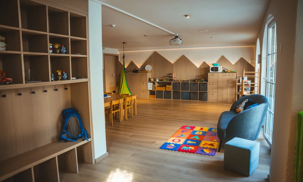 Käsestube melted - Resort La Ginabelle Zermatt Kinderspielzimmer mit Holzregalen, Spielzeug und bunter Spielmatte